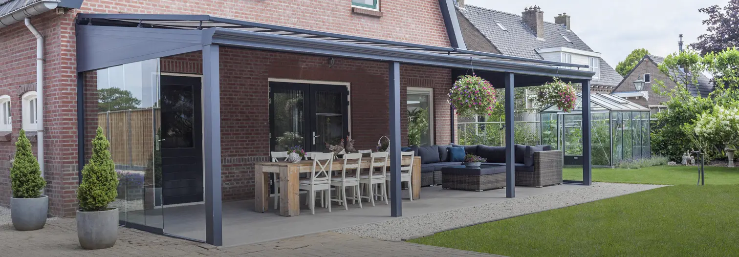Covered patio attached to a brick home with a glass roof, outdoor dining table, potted plants, and lounge seating