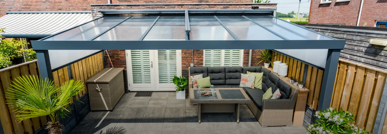 Modern aluminum patio cover with a glass roof over an outdoor seating area featuring wicker furniture and wooden fencing